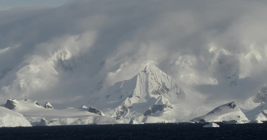 Magical snow covered mountains loom over dark moody ocean