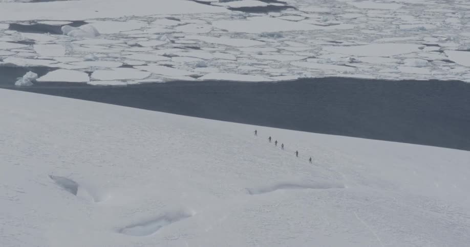 A line of people walking through a large plain of ice with crevasse