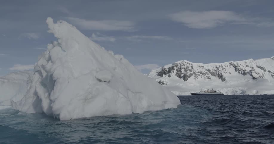 Large iceberg floating in a body of water with ship behind