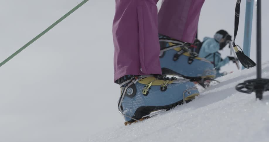 A low tight view of woman's feet climbing up a snowy mountain in crampons and ski boots
