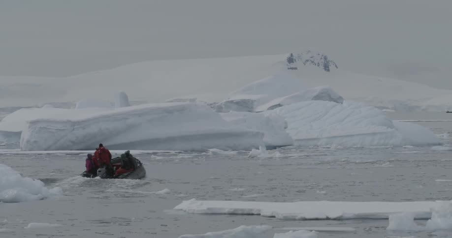 A boat filled with people travels toward an iceberg