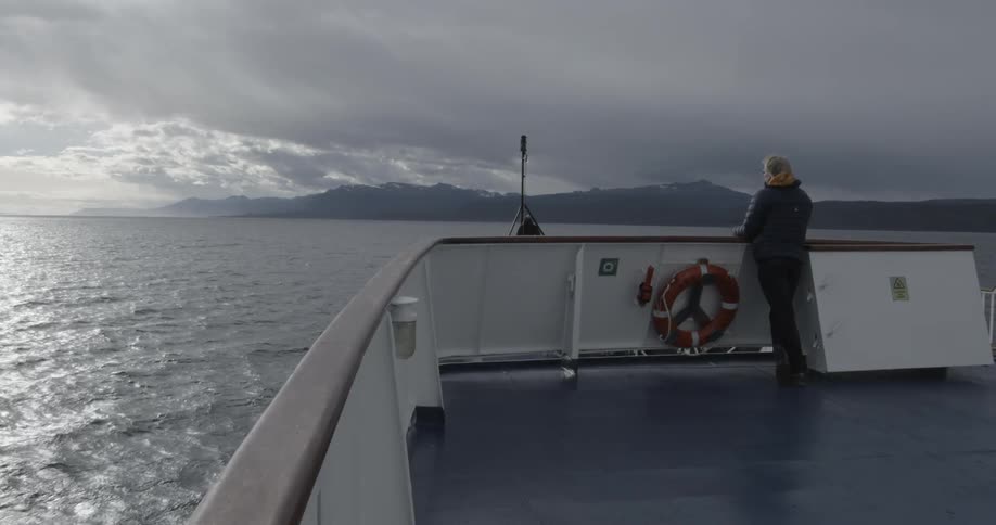A person is looking out towards dramatic clouds from a moving ship
