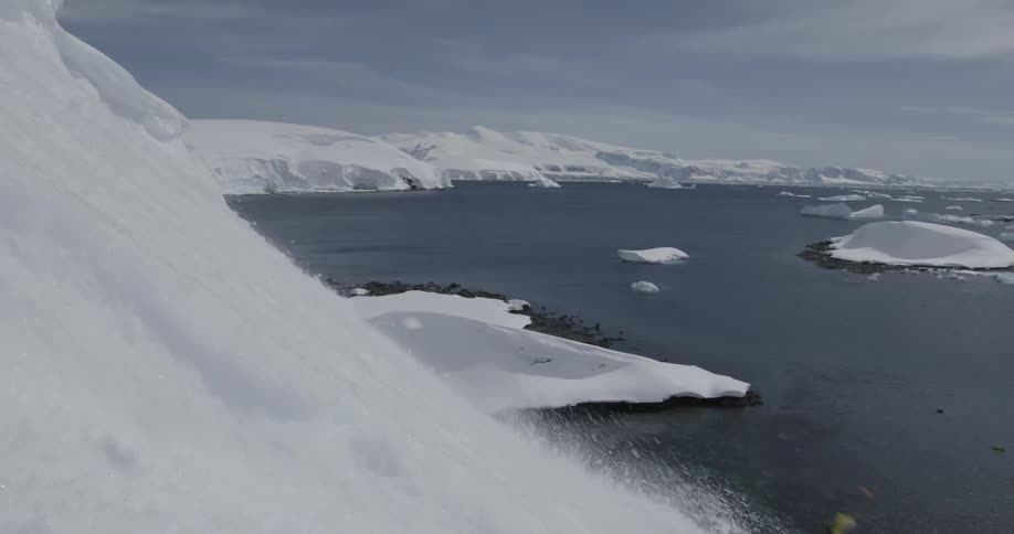 A skier wearing a heavy backpack skis down a steep slope through the frame to water