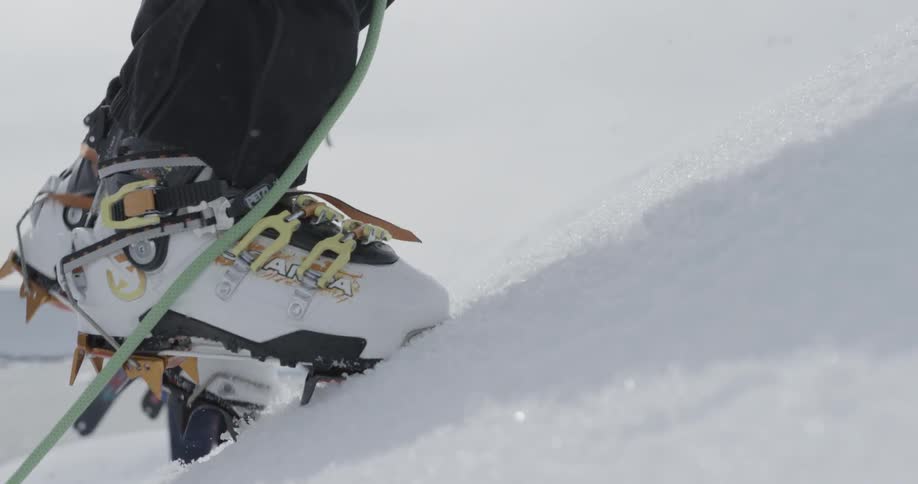 A lower view of legs, boots, crampons, pants and poles to climb the snow