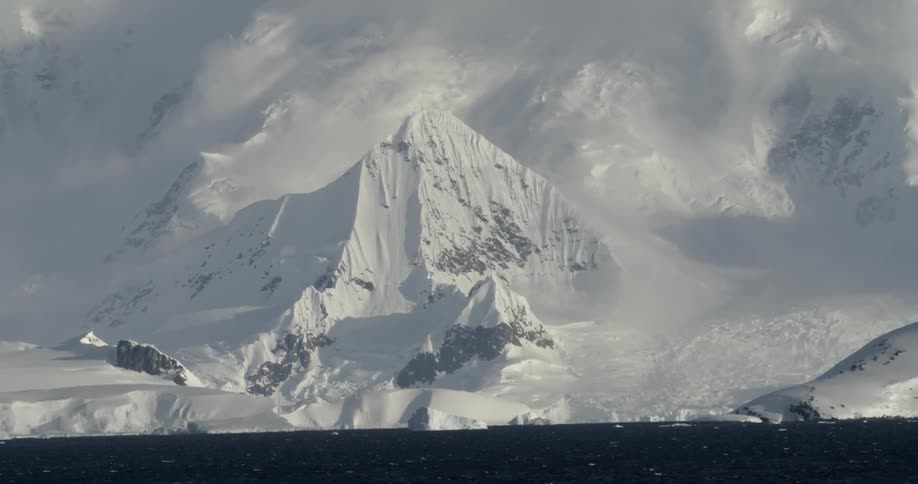 Large epic snow covered mountains rise out of the ocean