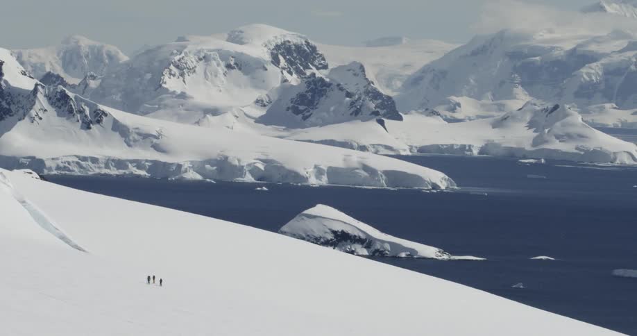 People are hiking in snowy mountains with icy water below