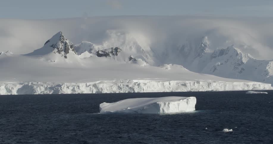 An epic scene of an Iceberg floating in Antarctica with Ice shelf and mountains behind