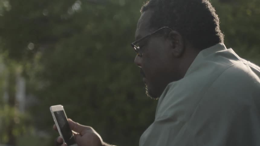 A man wearing glasses smiles at his phone before putting it away