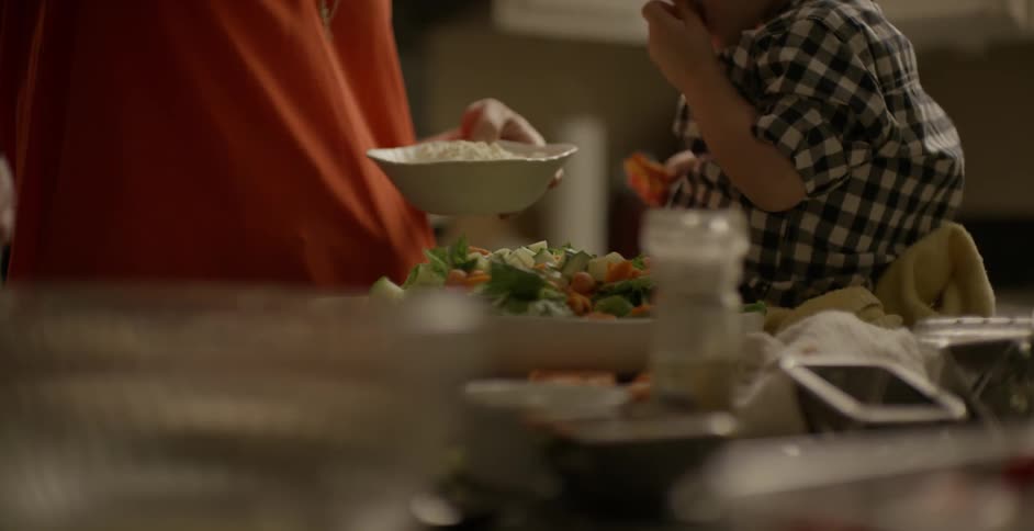 A person shows a child how to sprinkle cheese onto a salad