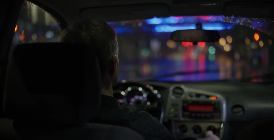 A driver takes a sip of a drink from the driver seat