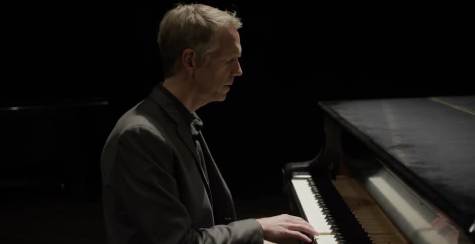 A man sits at a piano and begins to play