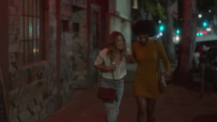 Two women laugh and walk down the street
