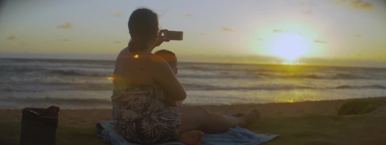 A woman holding a baby takes a picture of the sunrise