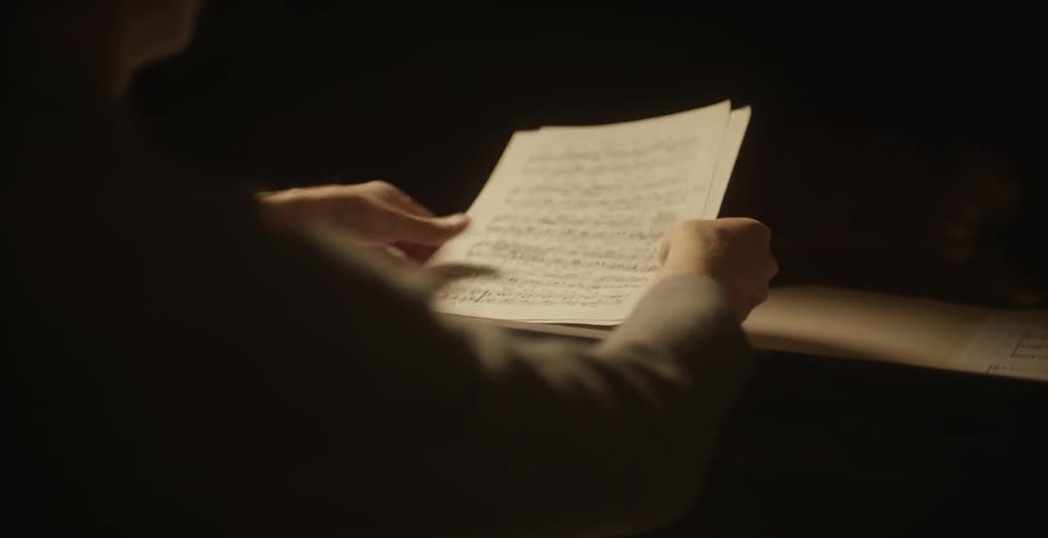 A man spreads out sheets of music on a piano