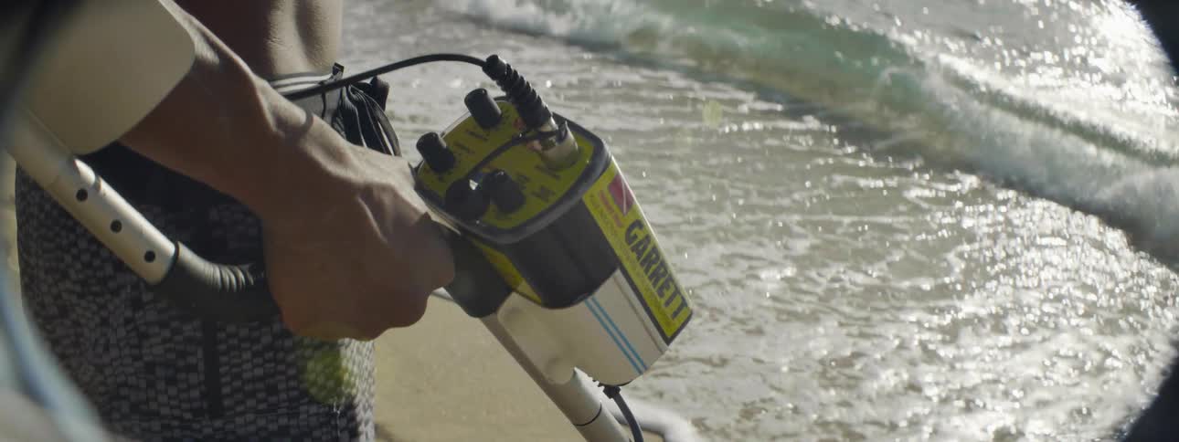 A person adjusts a metal detector at the beach