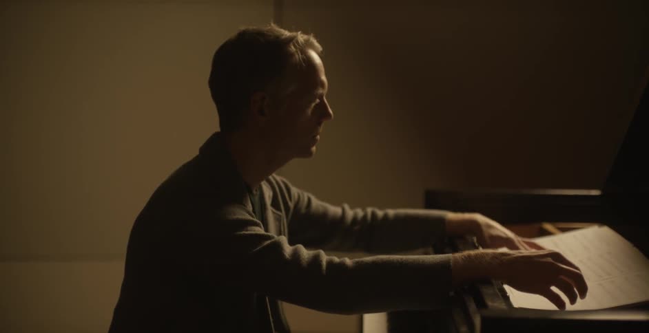 Man sits at a piano looking at sheet music