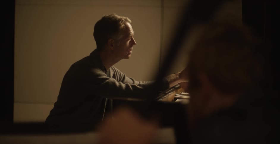Man looks through sheet music sitting at a piano