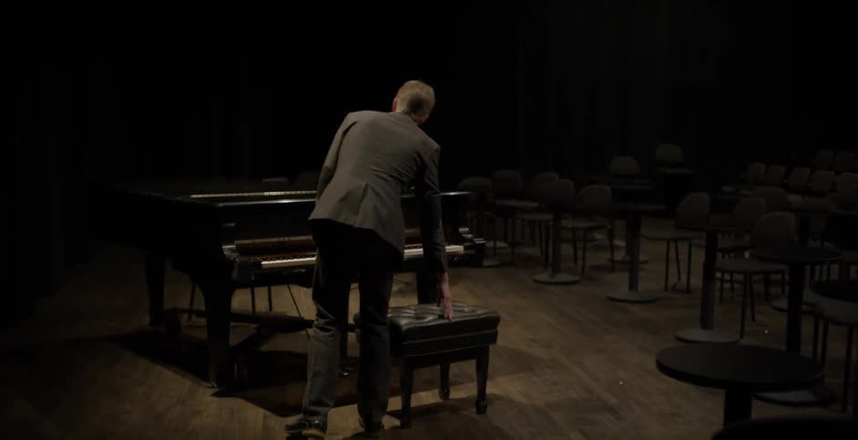 A man sits on a bench in front of a piano