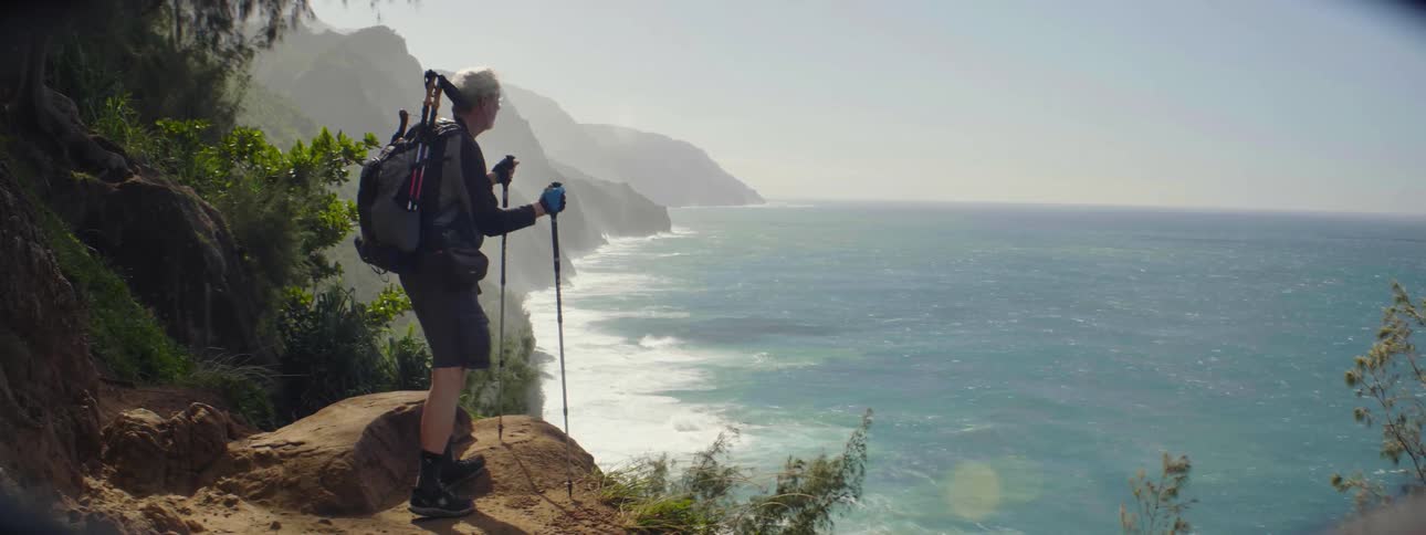 A man hikes to a ledge overlooking the ocean