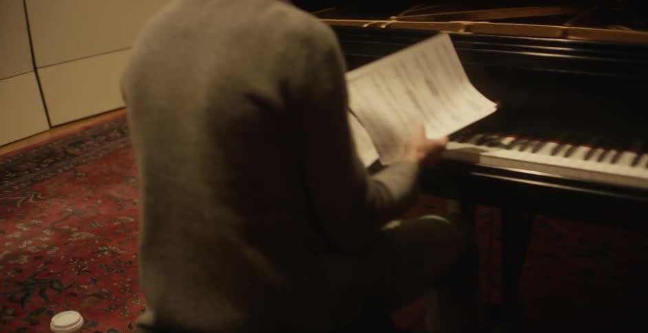 A man is sitting at a piano looking at sheet music