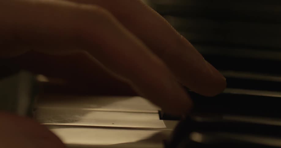 The fingers slowly press the black and white piano keys