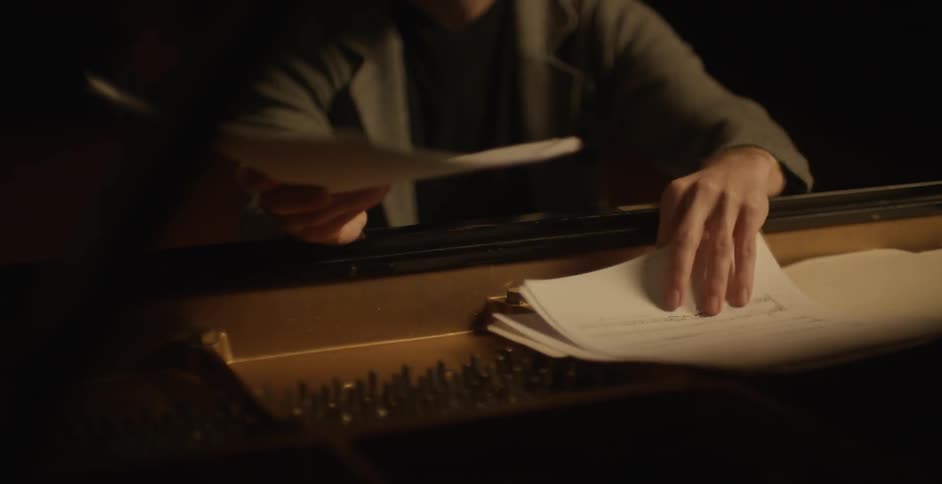 A man arranges paper on the top of a piano