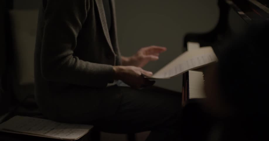 A man looks at sheets of music while sitting at a piano