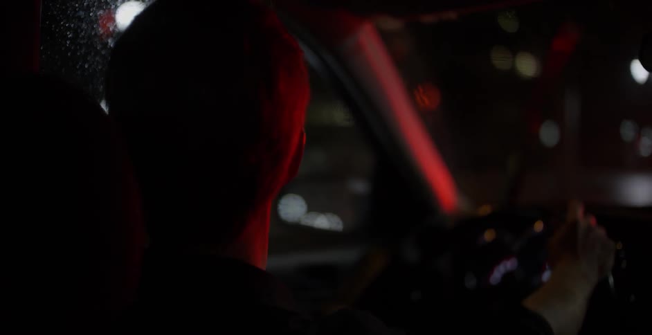 A man is driving at night using his windshield wipers