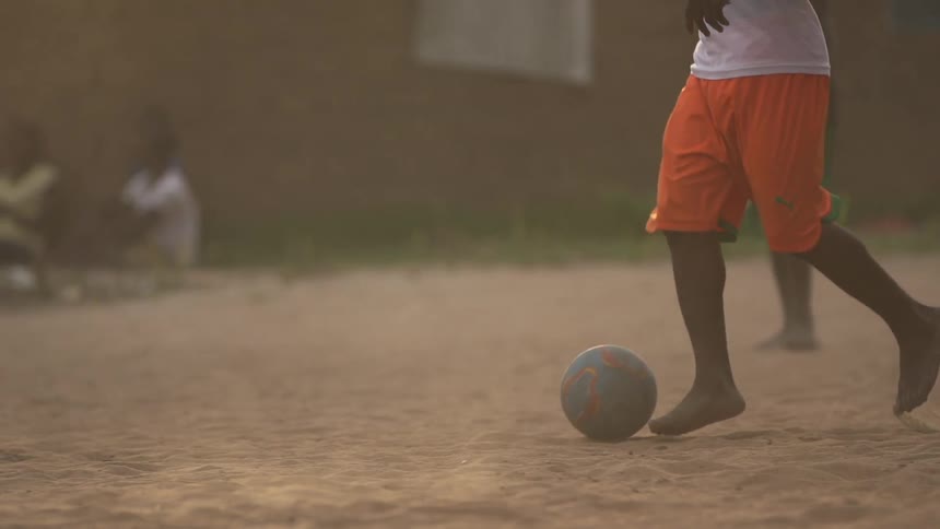 Barefoot boy kicking a soccer ball in the dirt