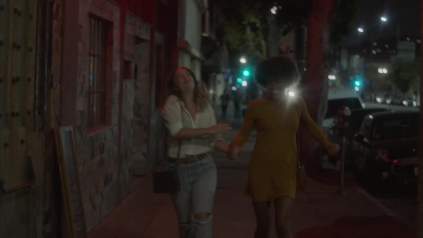 Two women holding hands laughing and running down a city street at night