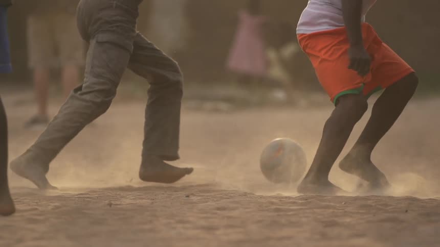 Barefoot boys playing soccer in a dusty area