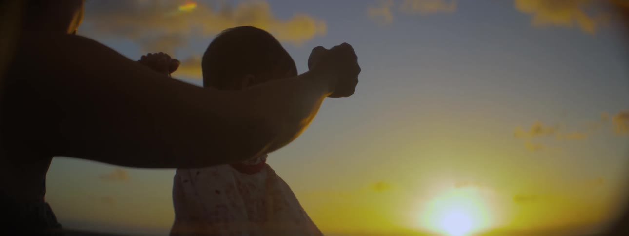 A woman holds her daughter on the beach at sunrise