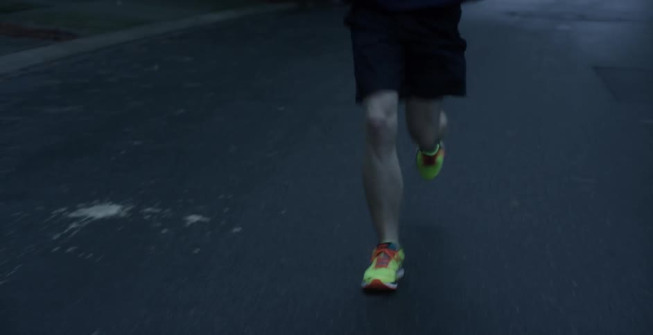 Hooded man running in a neighborhood at sunset