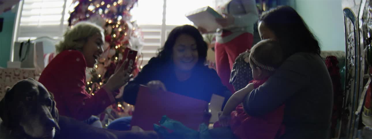 A family is sitting around the christmas tree opening gifts