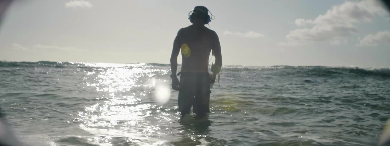 Man carrying a metal detector wades in the ocean