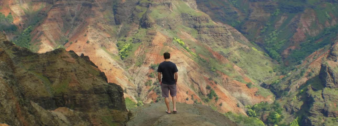 A man carefully steps down to a ledge overlooking a canyon