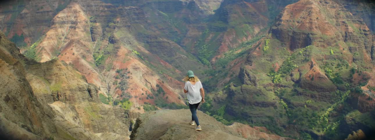 A woman in a white shirt jogs on a rocky path to a cliff
