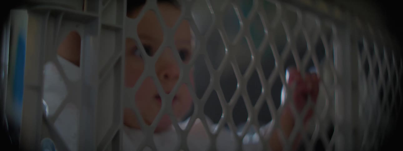 A baby tries to pull herself up using a baby gate