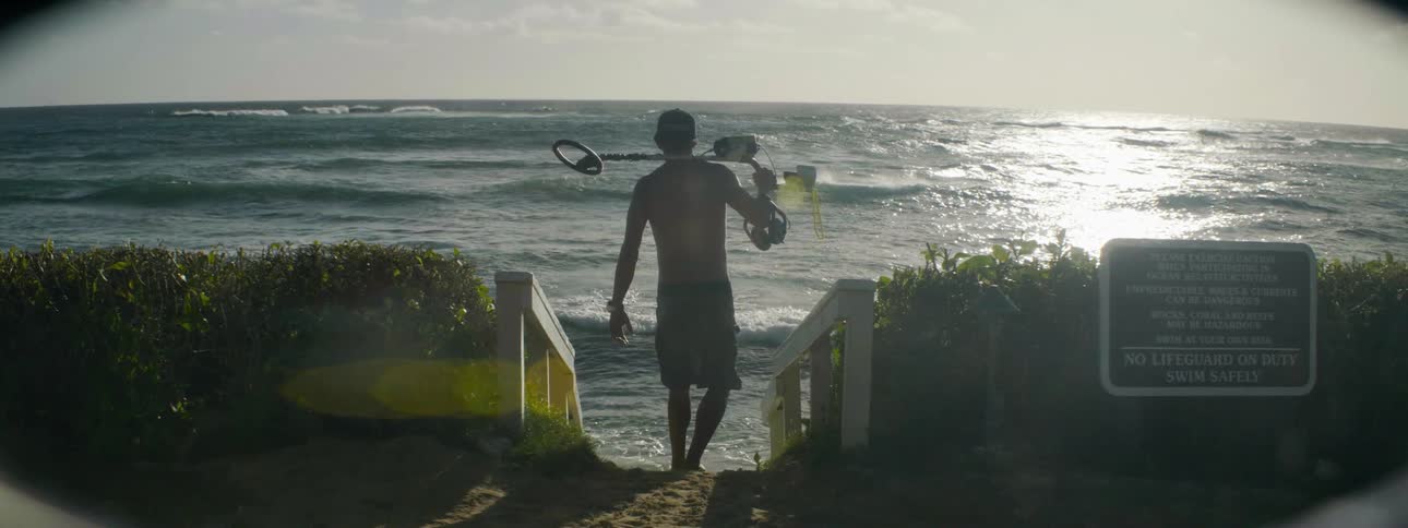 A man carries a metal detector towards the beach