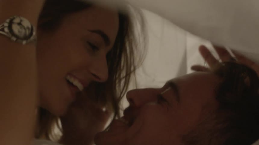A man and woman roll around in bed together under the sheets