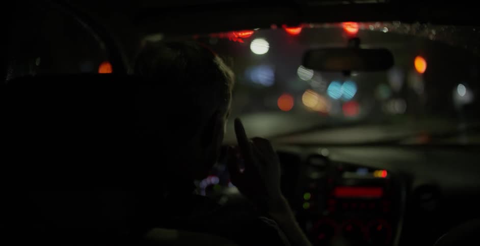A man waits in a car with the windshield wipers on