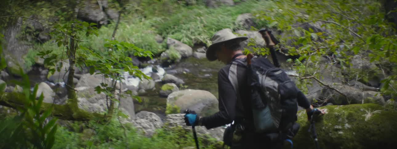 A man hikes a rocky trail near a stream