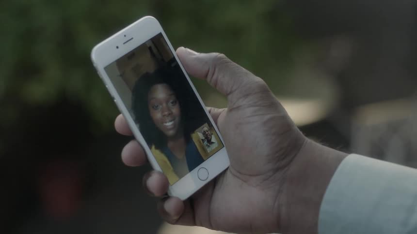 Person holding a phone that shows a woman smiling and talking