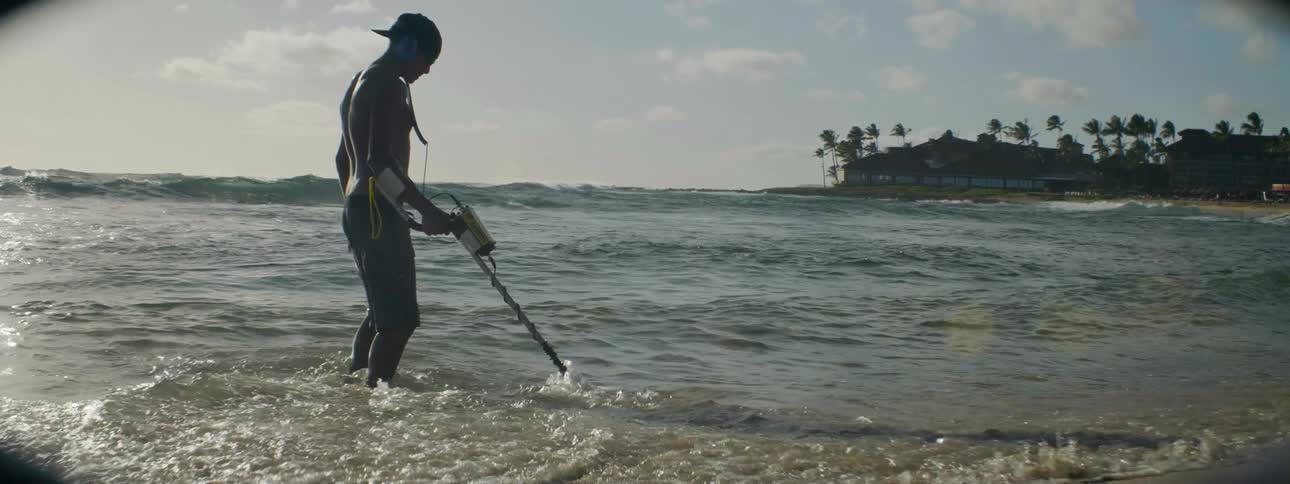 A man is using a metal detector at the beach during the day
