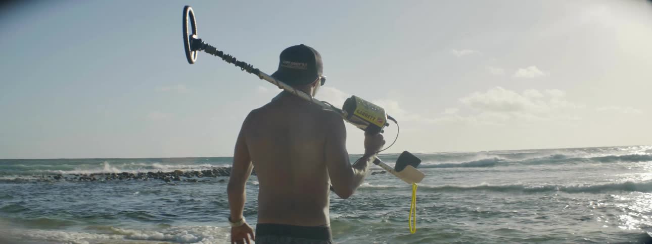 A man carrying a metal detector walks on the beach