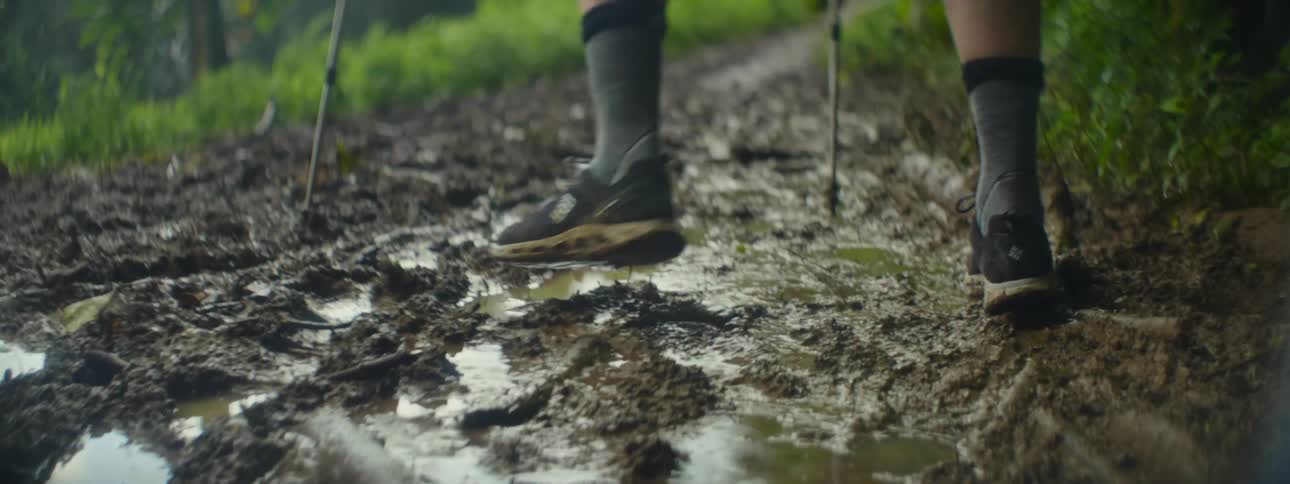 Person walking on a muddy path using walking sticks