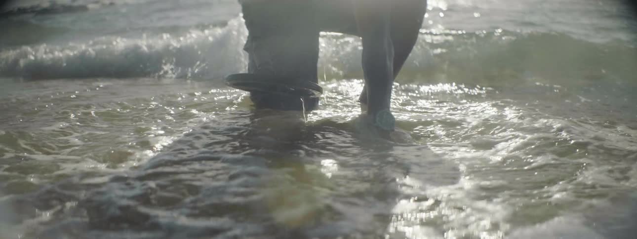A man using a metal detector kneels down to dig in the sand
