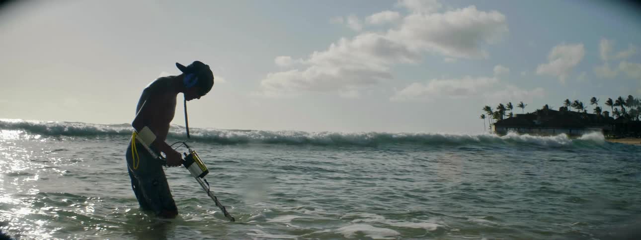 A man is using a metal detector in the shore