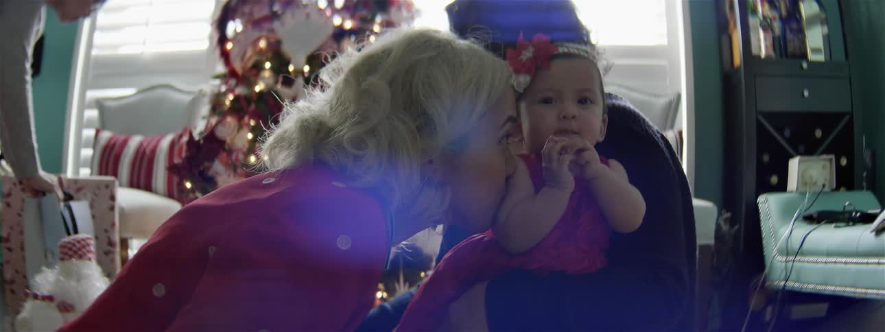 A woman kisses a baby dressed in christmas clothes