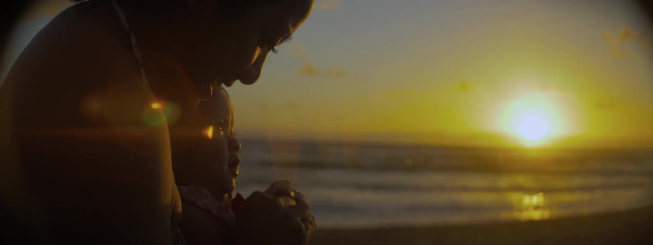 Woman holding at child looking down at the beach at sunset